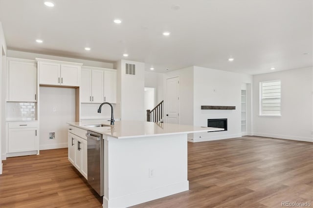 8346 Cokedale Cir, Littleton, CO 80125 - kitchen featuring stainless steel dishwasher, white cabinetry, light wood-type flooring, an island with sink, and light countertops