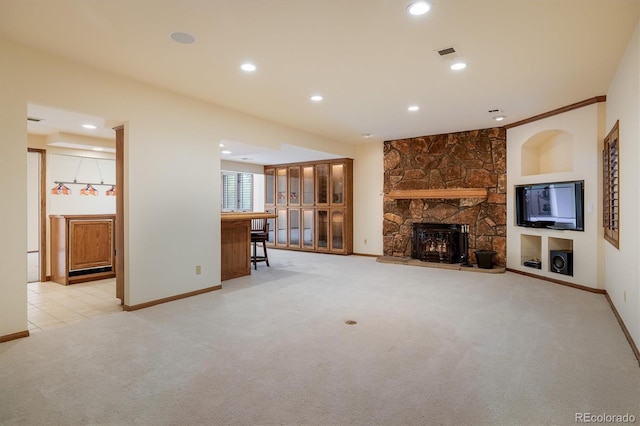 unfurnished living room with bar, a stone fireplace, built in features, and light colored carpet