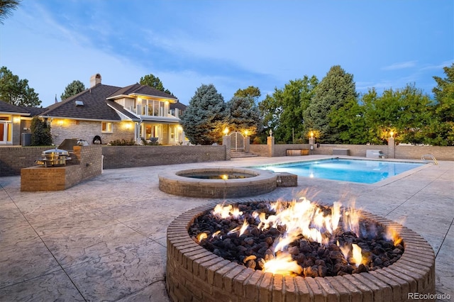 pool at dusk featuring exterior kitchen, a patio, an in ground hot tub, and a fire pit