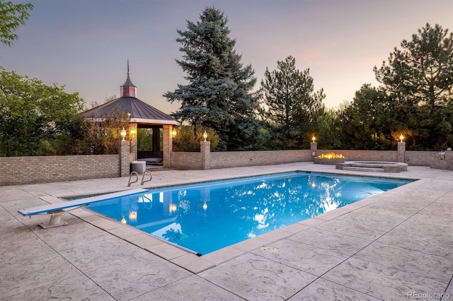 pool at dusk with a hot tub, a gazebo, a diving board, and a patio area