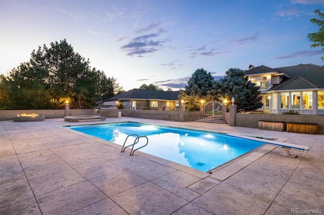 pool at dusk featuring a diving board, a patio area, and a jacuzzi