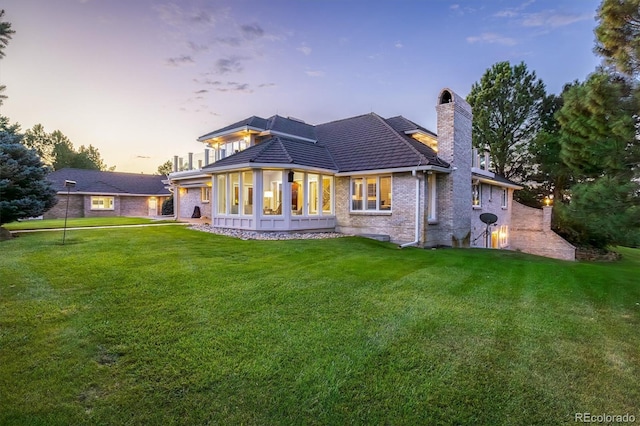 back house at dusk featuring a sunroom and a lawn