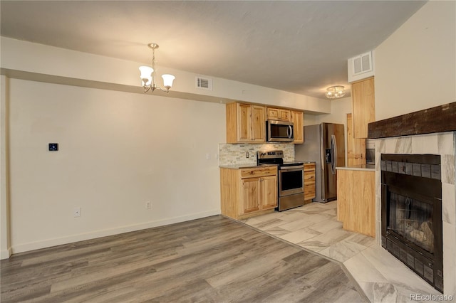 kitchen featuring appliances with stainless steel finishes, pendant lighting, decorative backsplash, a tiled fireplace, and an inviting chandelier