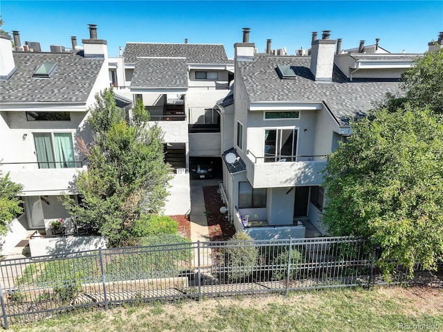 exterior space featuring stucco siding, a chimney, a shingled roof, a balcony, and a fenced front yard