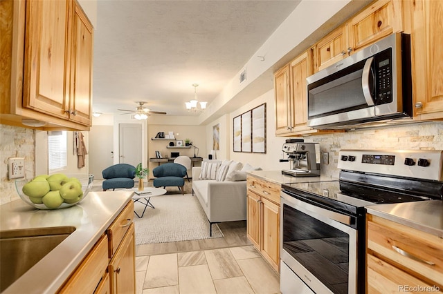 kitchen with tasteful backsplash, ceiling fan with notable chandelier, stainless steel appliances, light brown cabinets, and decorative light fixtures