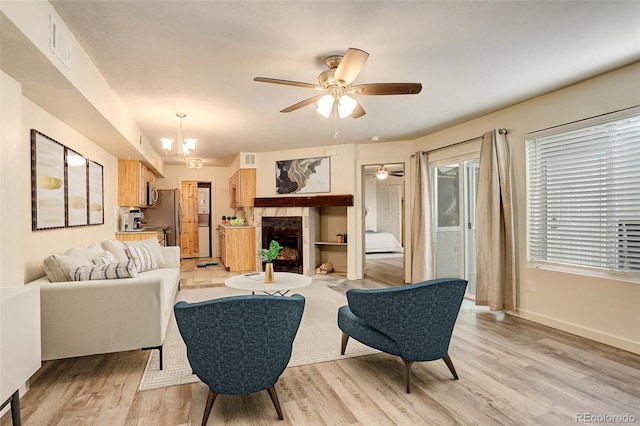 living room featuring ceiling fan with notable chandelier, a tile fireplace, and light wood-type flooring