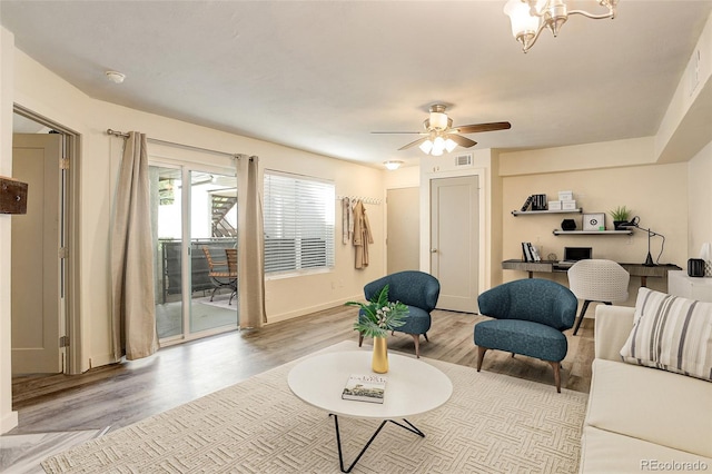 living room with light wood-type flooring, visible vents, baseboards, and ceiling fan with notable chandelier