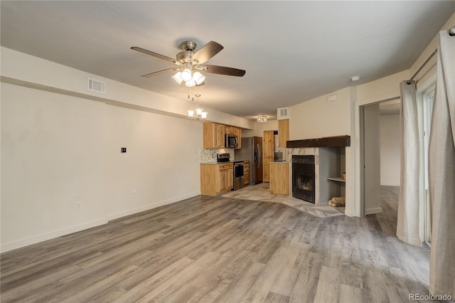 unfurnished living room with light wood finished floors, a tiled fireplace, visible vents, and ceiling fan with notable chandelier