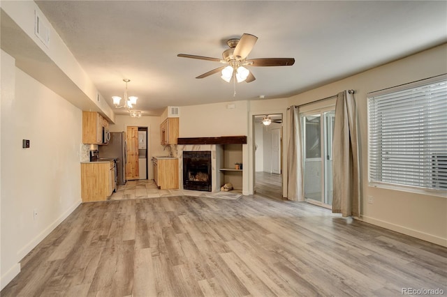 unfurnished living room with light wood finished floors, visible vents, baseboards, and ceiling fan with notable chandelier