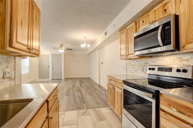 kitchen with ceiling fan with notable chandelier, a sink, stainless steel appliances, visible vents, and backsplash