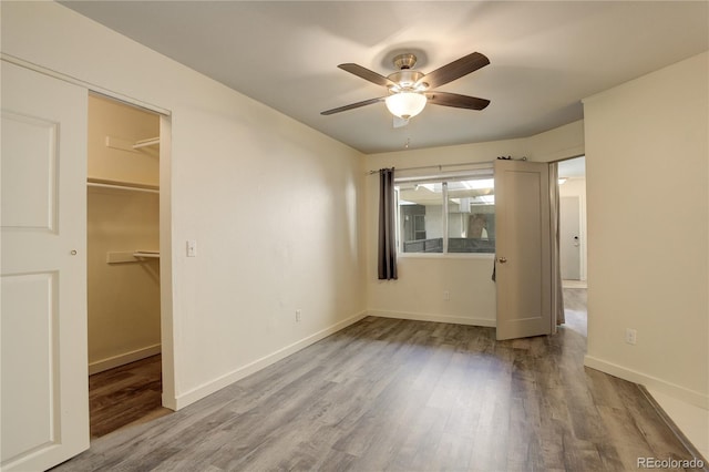 unfurnished bedroom with wood finished floors, a ceiling fan, a closet, baseboards, and a spacious closet