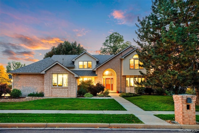 view of front of house with a front lawn, a shingled roof, and brick siding