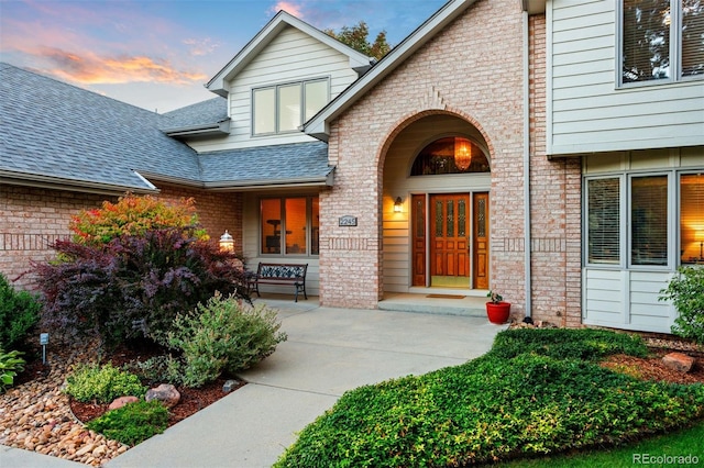 property entrance featuring brick siding and roof with shingles