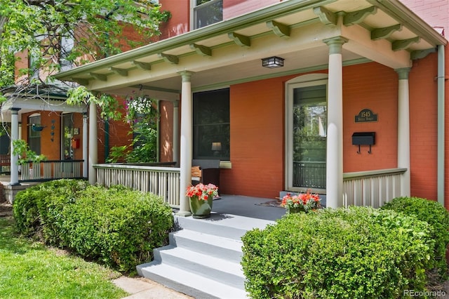 view of exterior entry with a porch and brick siding