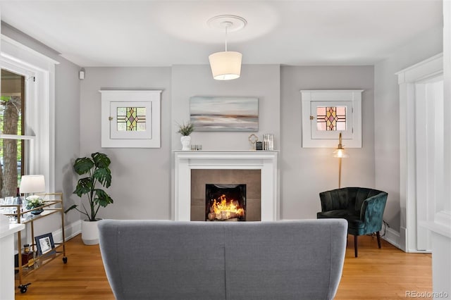 living area with wood finished floors, a tiled fireplace, and baseboards