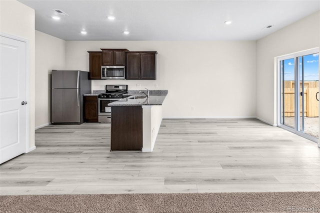 kitchen with dark brown cabinets, stainless steel appliances, dark stone counters, sink, and light hardwood / wood-style floors