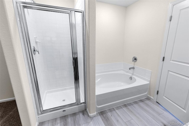 bathroom with a garden tub, baseboards, wood finished floors, and a stall shower