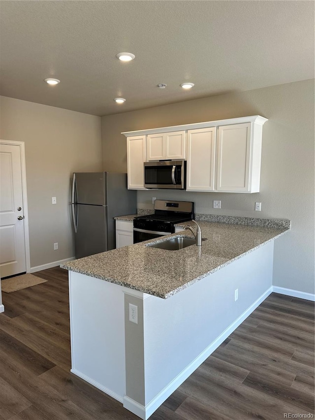 kitchen featuring white cabinetry, appliances with stainless steel finishes, a peninsula, light stone countertops, and dark wood-style flooring