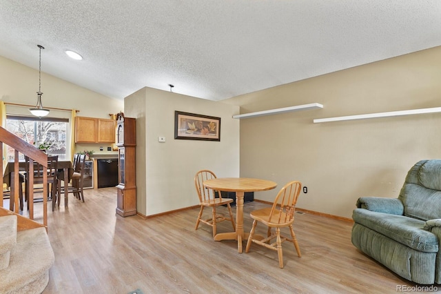 dining room with lofted ceiling, baseboards, light wood finished floors, and a textured ceiling