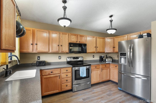 kitchen with a sink, light wood-style flooring, pendant lighting, and stainless steel appliances