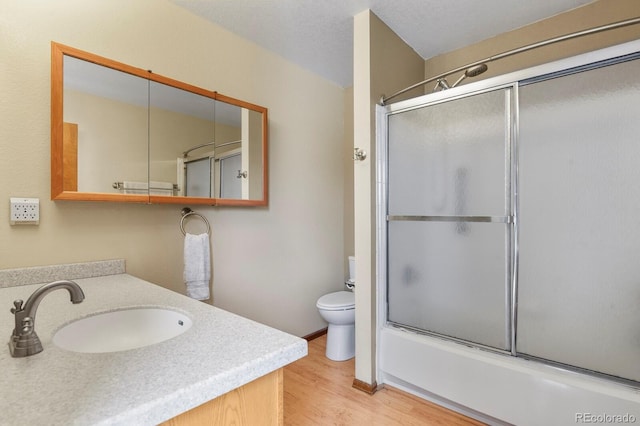 bathroom featuring enclosed tub / shower combo, toilet, wood finished floors, and vanity