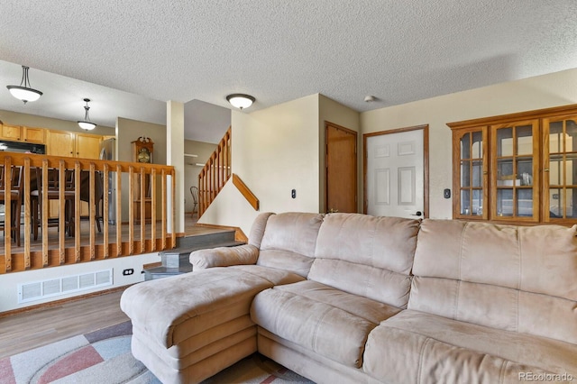 living area featuring stairway, wood finished floors, visible vents, and a textured ceiling