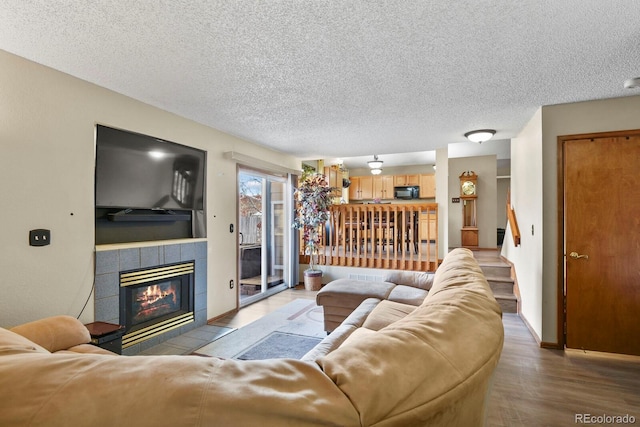 living area with a textured ceiling, wood finished floors, and a tile fireplace