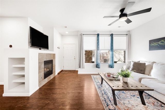 living room featuring ceiling fan, dark wood-type flooring, built in features, and a tiled fireplace