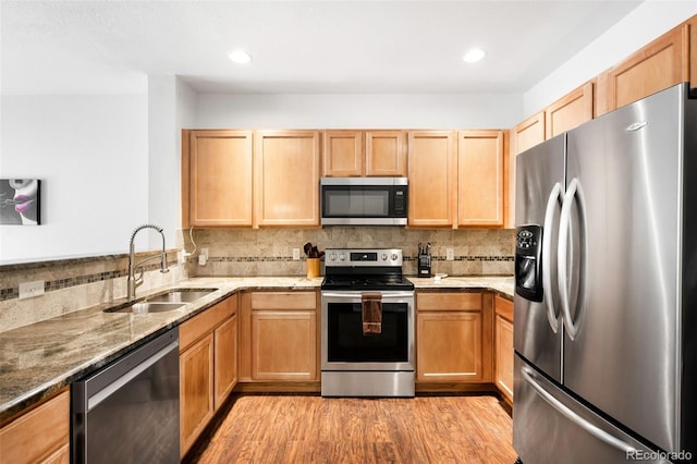 kitchen featuring light stone countertops, appliances with stainless steel finishes, sink, backsplash, and light hardwood / wood-style flooring