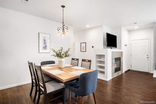 dining room with built in shelves, dark hardwood / wood-style floors, a fireplace, and a notable chandelier