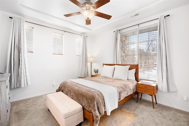 bedroom with ceiling fan, a raised ceiling, light colored carpet, and multiple windows