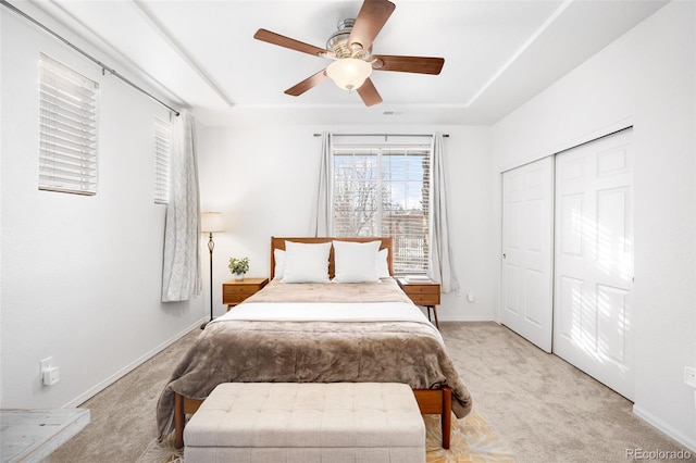 carpeted bedroom with a closet, ceiling fan, and a tray ceiling