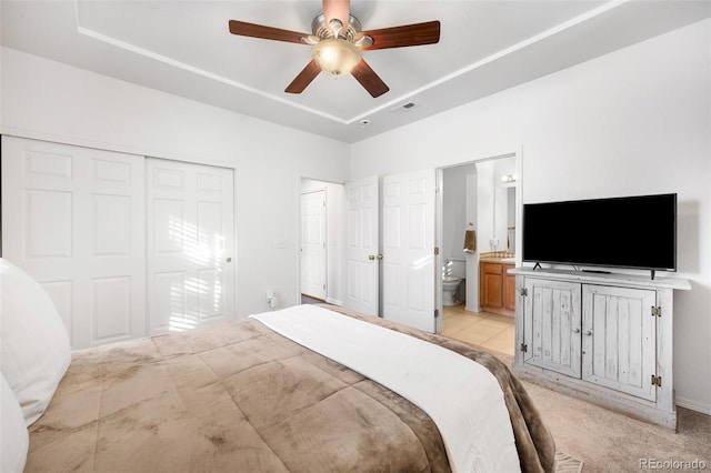 bedroom with ceiling fan, light carpet, connected bathroom, and a tray ceiling