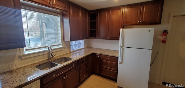 kitchen featuring light tile patterned floors, white refrigerator, light stone countertops, and sink