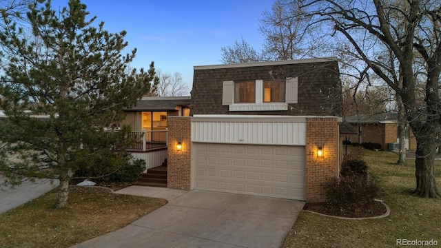 view of front facade featuring concrete driveway, roof with shingles, brick siding, and mansard roof