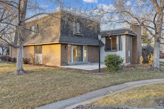 view of front of home featuring a patio, mansard roof, brick siding, roof with shingles, and a front yard