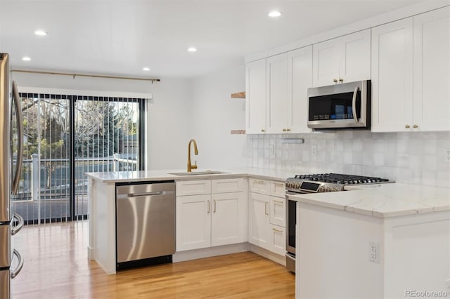 kitchen featuring stainless steel appliances, a peninsula, a sink, and white cabinets