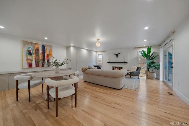 living room with a lit fireplace, recessed lighting, visible vents, and light wood-style floors