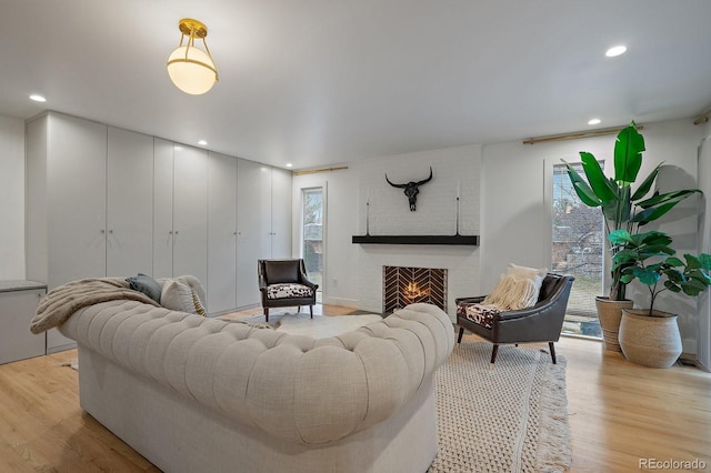 living area featuring light wood finished floors, a brick fireplace, and recessed lighting