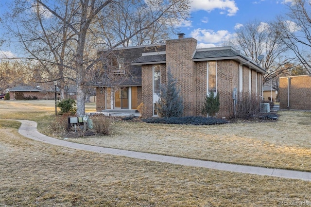 view of front of property with central air condition unit, brick siding, roof with shingles, a chimney, and a front yard