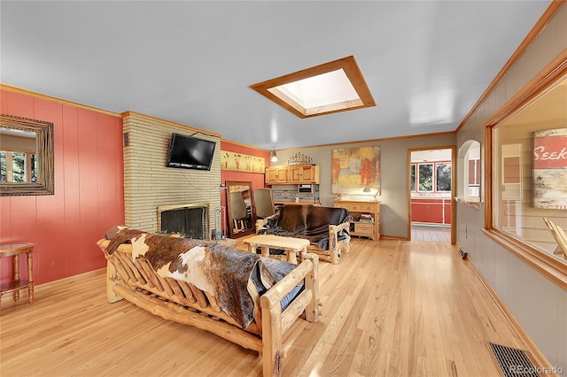 living room with light wood-type flooring, a skylight, crown molding, and a brick fireplace