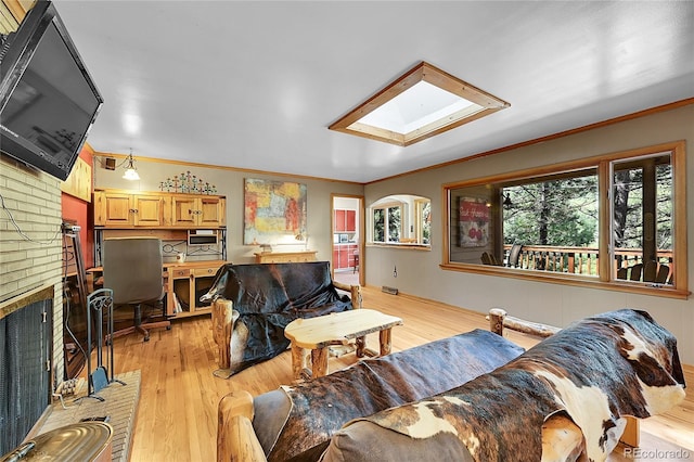 living room featuring a fireplace, a skylight, light hardwood / wood-style floors, crown molding, and brick wall