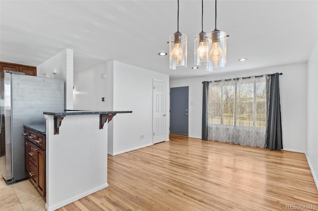 kitchen with stainless steel refrigerator, decorative light fixtures, a breakfast bar area, and light hardwood / wood-style flooring