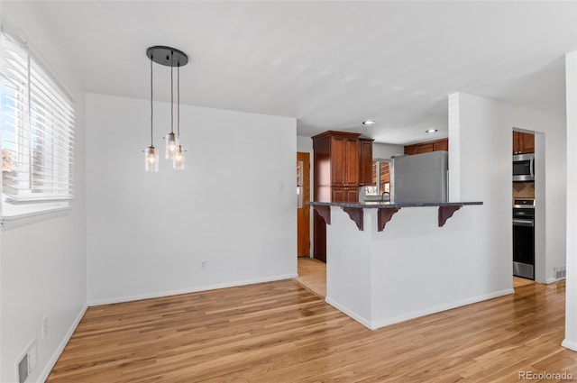 kitchen with stainless steel appliances, a wealth of natural light, a kitchen breakfast bar, and decorative light fixtures