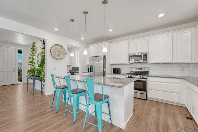 1066 S Eaton Park Ct, Aurora, CO 80018 - kitchen featuring stainless steel appliances, a kitchen island, light wood-style flooring, decorative backsplash, and a breakfast bar area