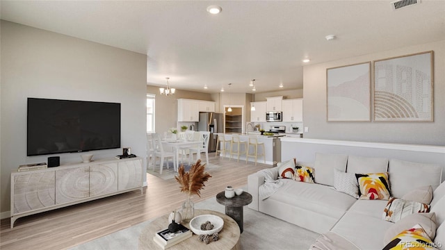 living area with light wood-type flooring, visible vents, a notable chandelier, and recessed lighting