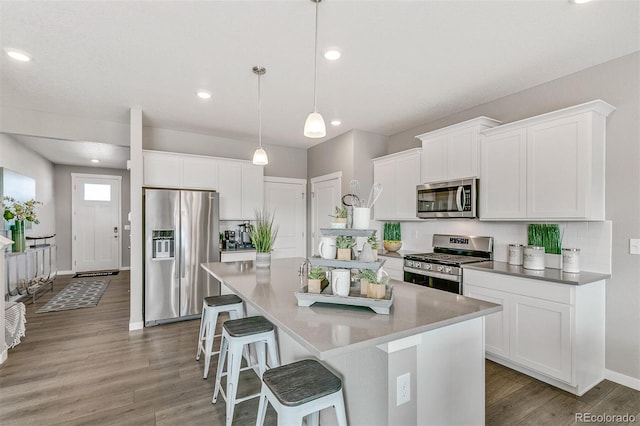 kitchen featuring appliances with stainless steel finishes, hanging light fixtures, wood-type flooring, an island with sink, and white cabinets