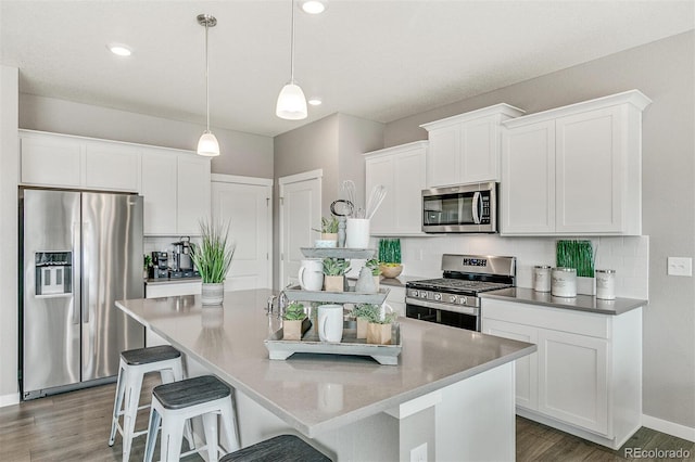 kitchen featuring hardwood / wood-style flooring, a kitchen island with sink, stainless steel appliances, white cabinets, and decorative light fixtures