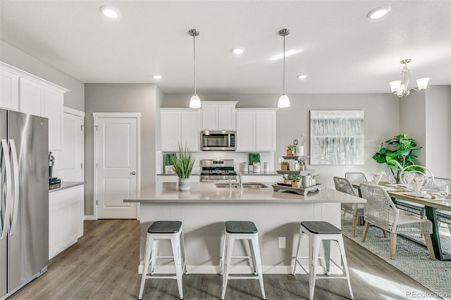 kitchen featuring appliances with stainless steel finishes, white cabinets, a center island with sink, decorative light fixtures, and light wood-type flooring