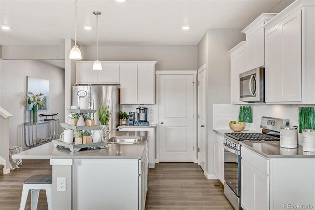 kitchen with pendant lighting, sink, appliances with stainless steel finishes, white cabinets, and a center island with sink